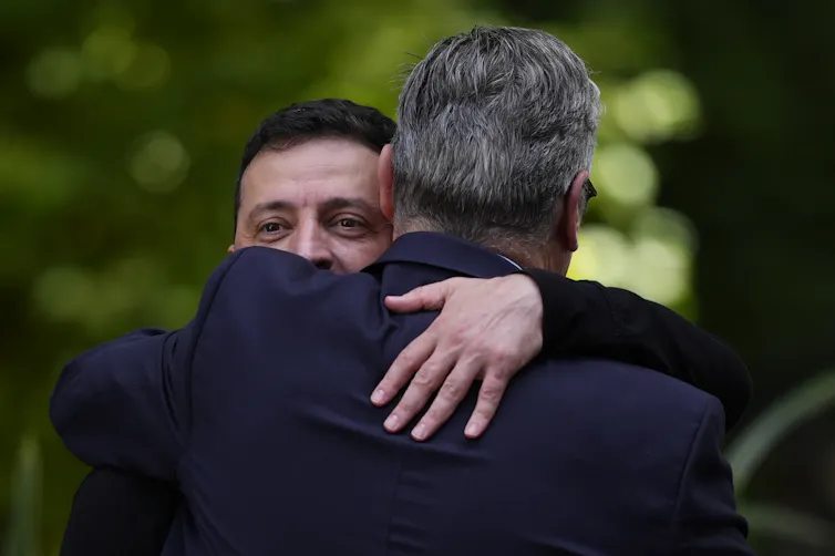 Two men in dark clothes hugging each other.