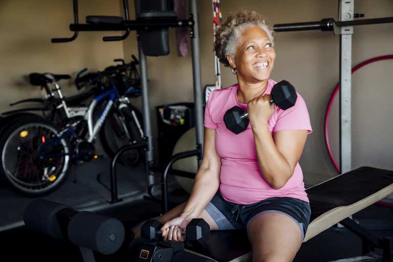 Smiling older woman lifting dumbells at the gym.
