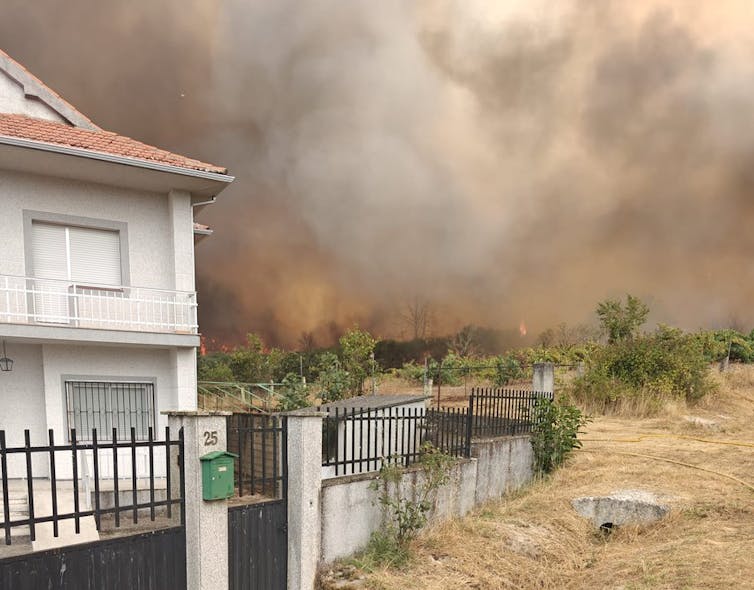 Una casa de pueblo y de fondo el humo y las llamas de un incendio