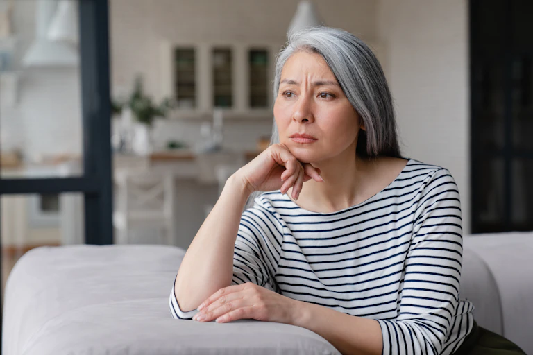 Une femme aux cheveux partiellement gris, vêtue d'une chemise rayée, l'air pensif.