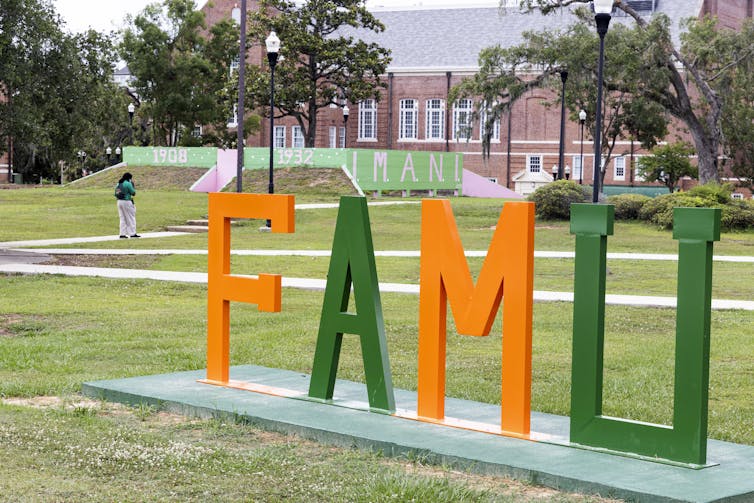 Orange and green letters spell out FAMU on a college campus.