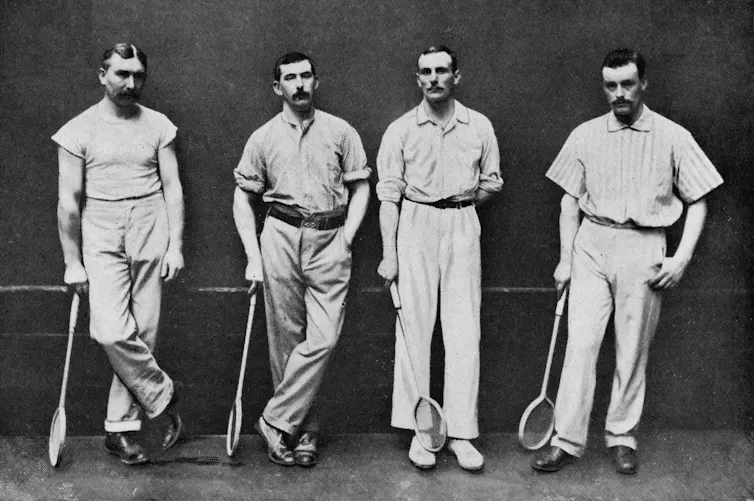 Black-and-white photo of four men in shirts, slacks and shoes holding squash rackets
