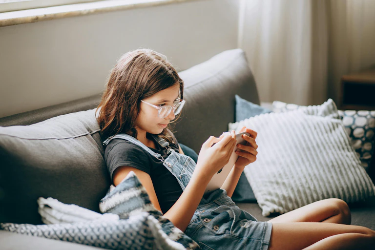A girl sits on a couch with a tablet.