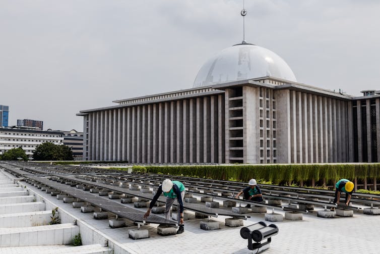 Workers lay solar panels near a mosque