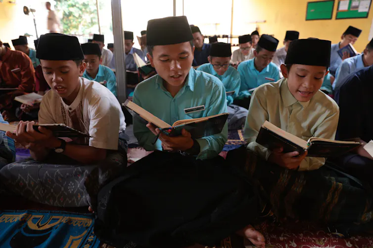 Para siswa laki-laki di sekolah Islam sedang membaca dari sebuah buku.