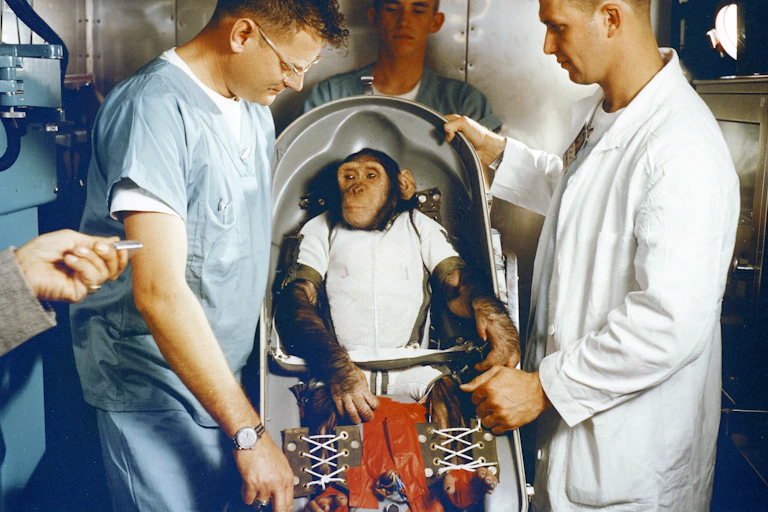 Ham, the chimpanzee, in his capsule, with his minders.