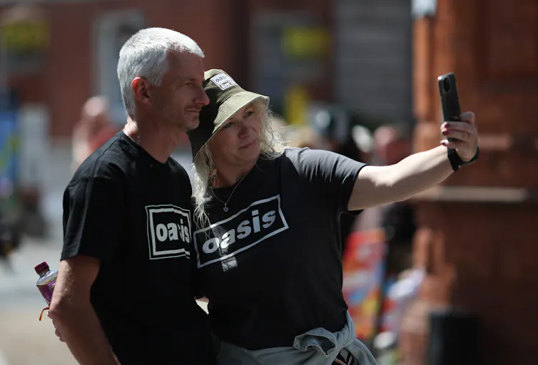 middle-aged couple wearing oasis t-shirts taking a selfie outside the concert.