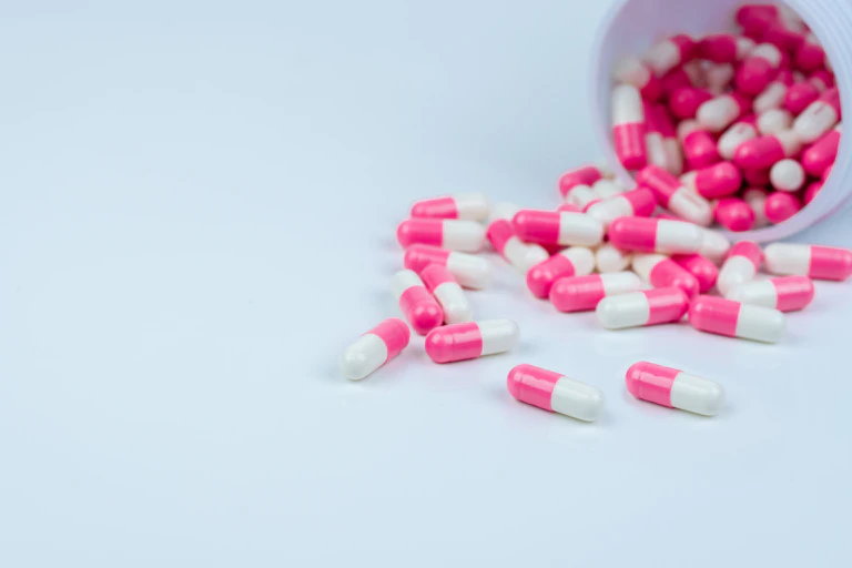 Pink and white pills spilling out of bottle.
