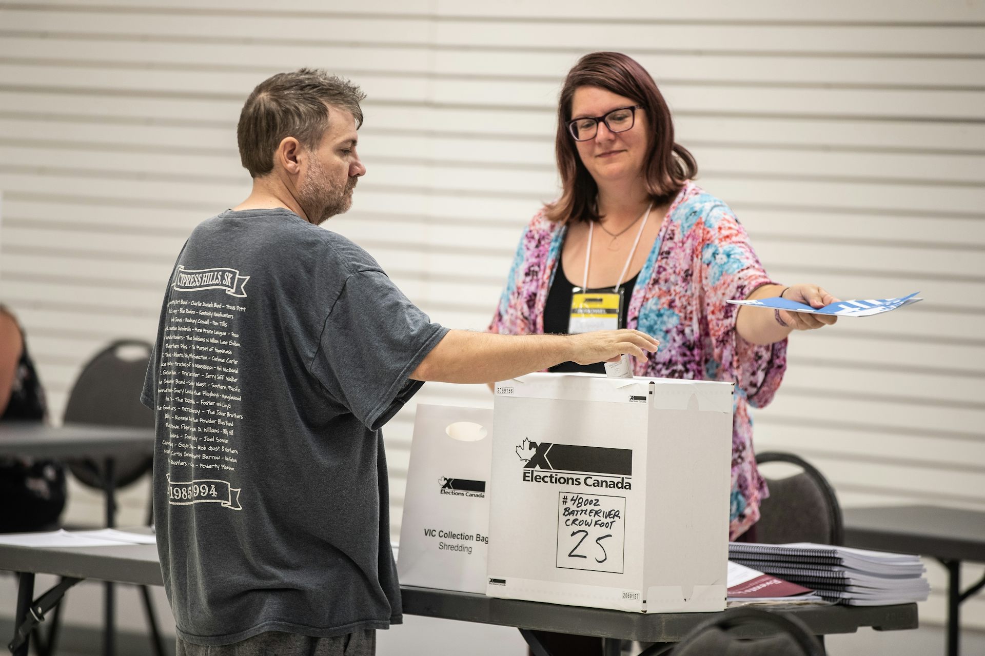 El hombre en las bolsas de camisetas inserta la votación en la caja como una sonriente trabajadora electoral parada cerca.