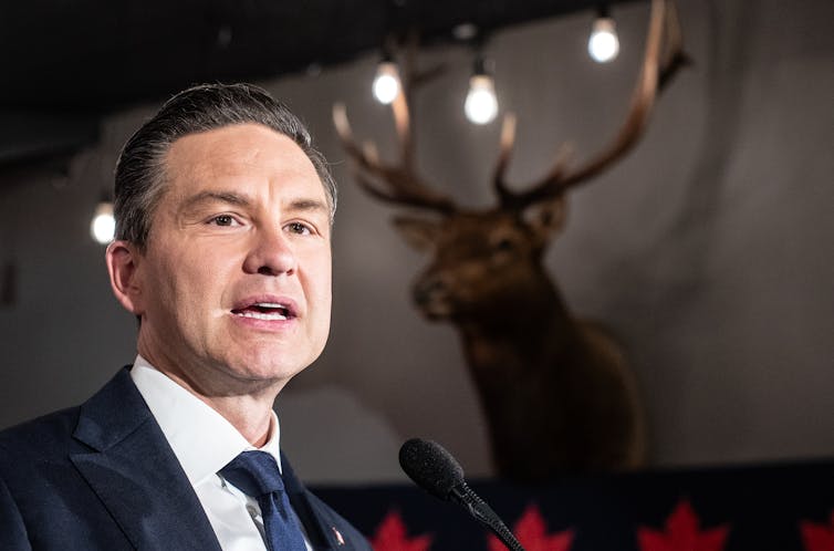 El hombre de cabello oscuro habla con las cabezas de golpe del sendero en la pared detrás de él.