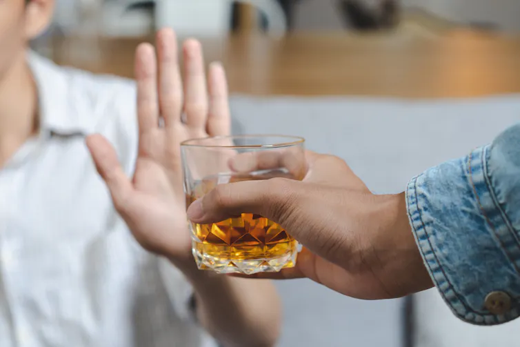 A person offering a drink and another refusing the drink.