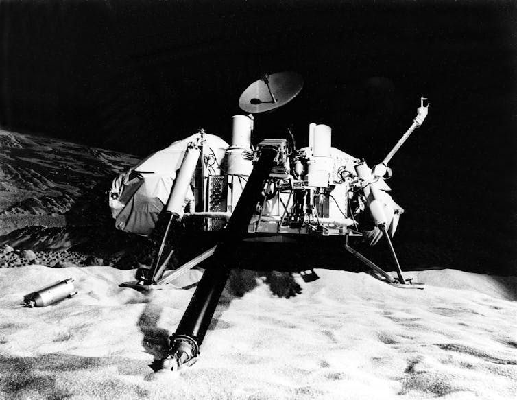 A small, low to the ground spacecraft with an antenna disk pointing upwards, resting on a rocky surface.