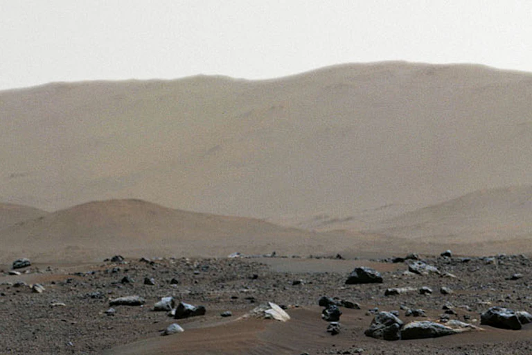 The dusty, rocky surface of Mars, with a mountainlike ridge in the background.