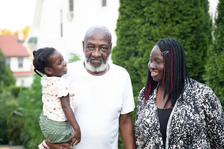A Black man holds a smiling girl while standing next to a younger Black woman.