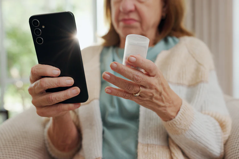 A person holding a bottle of medicines and a smartphone, looking up information