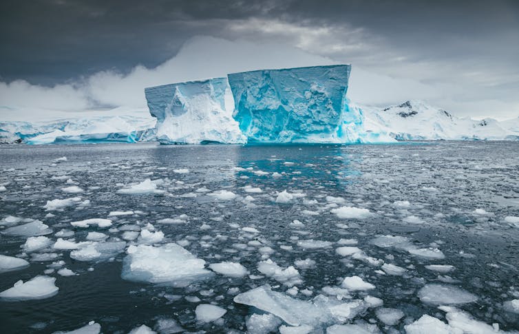 antarctica, iceshelf with blue ice looming at back and sea ice at the front over water.