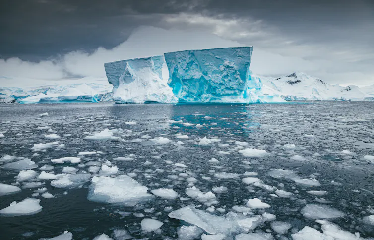 antarctica, iceshelf with blue ice looming at back and sea ice at the front over water.