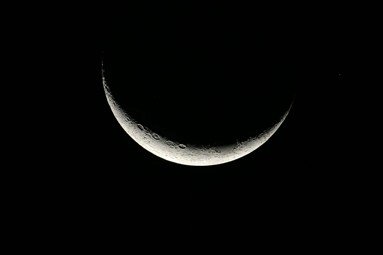 A crescent moon zoomed in so craters are visible, with most of the moon completely blending into the black background.