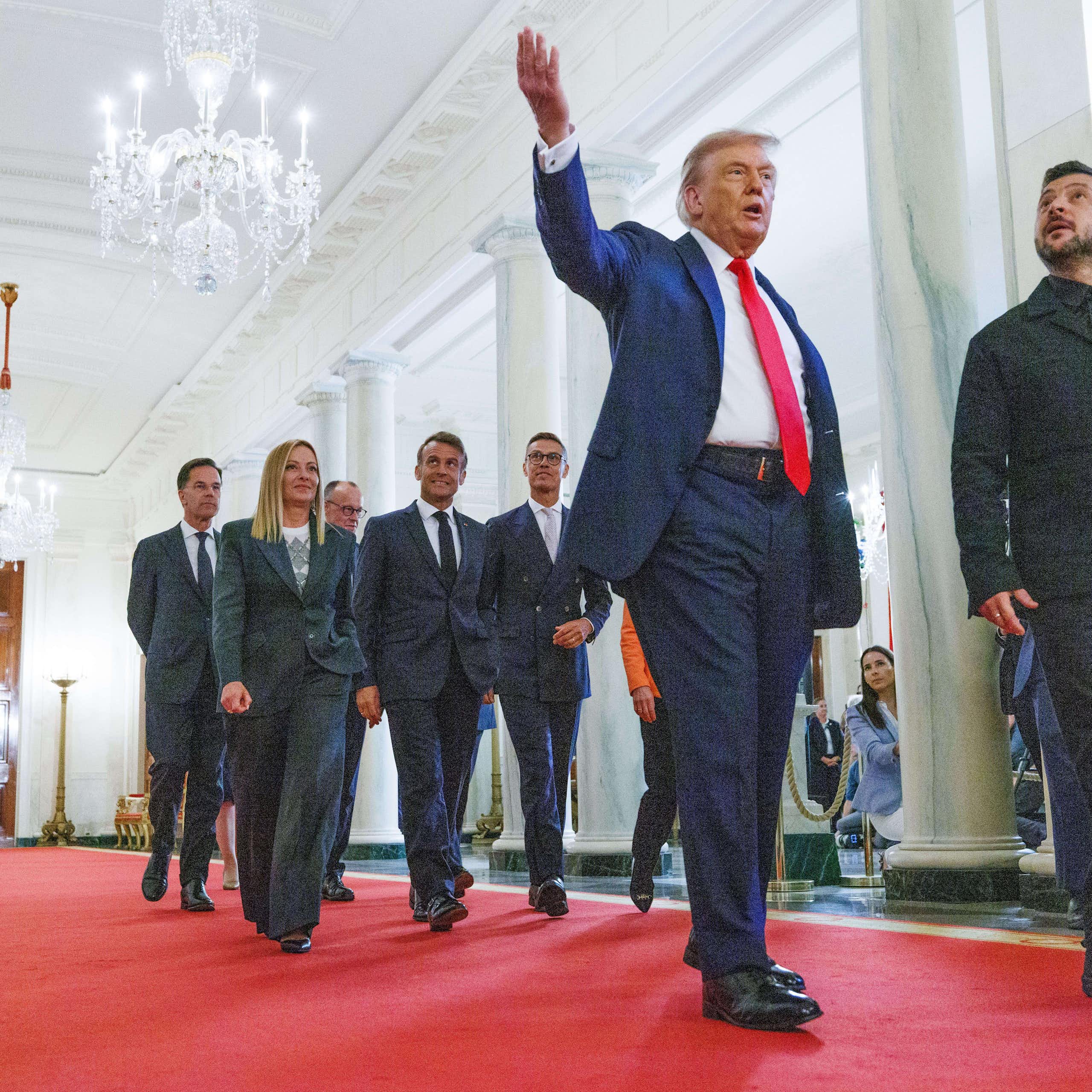 US president, Donald Trump, points to the ceiling as he walks down a White House corridor with Ukrainian president Volodymyr Zelensky. A group of aides follows.