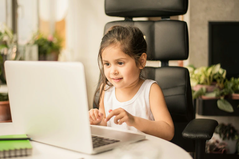 a young girl sits at a laptop