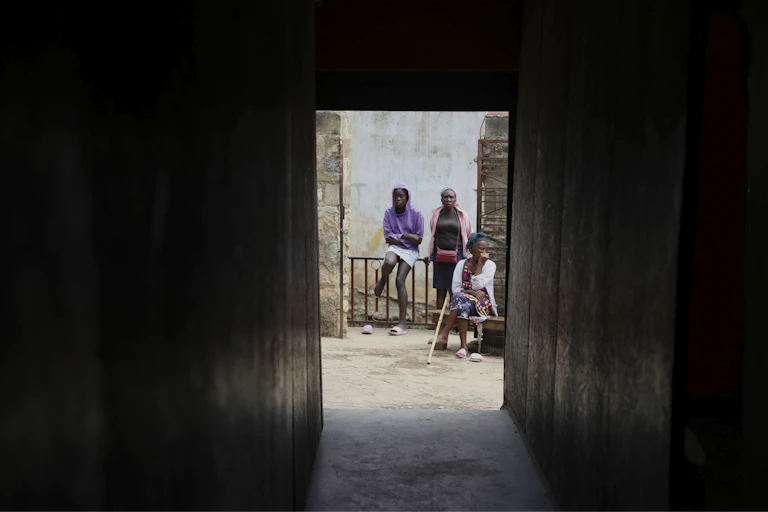 Three people are photographed sitting outside through the darkened door and hallway of a church.