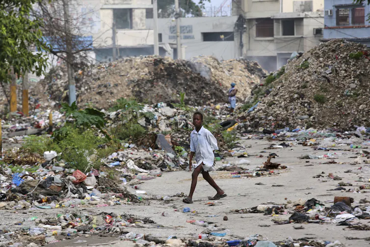 A young person crosses a garbage-strewn street.