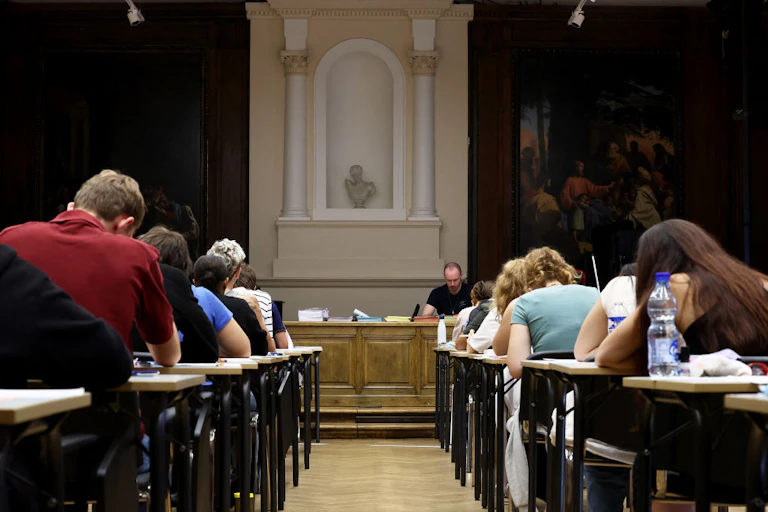 Rows of students bent over their desks, viewed from the back, with a small statue displayed at the front of the room.