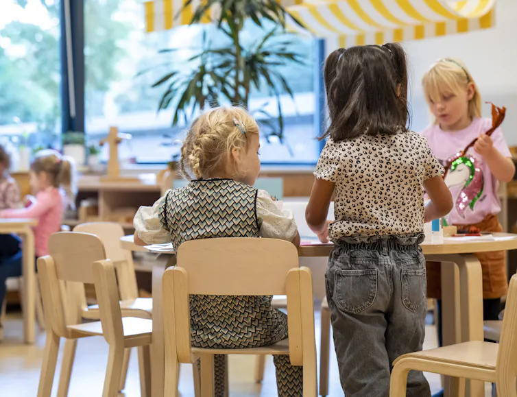 Toddlers engaged in an activity at a wooden table in a classroom.