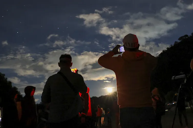 People hold cameras up to a darkening sky.