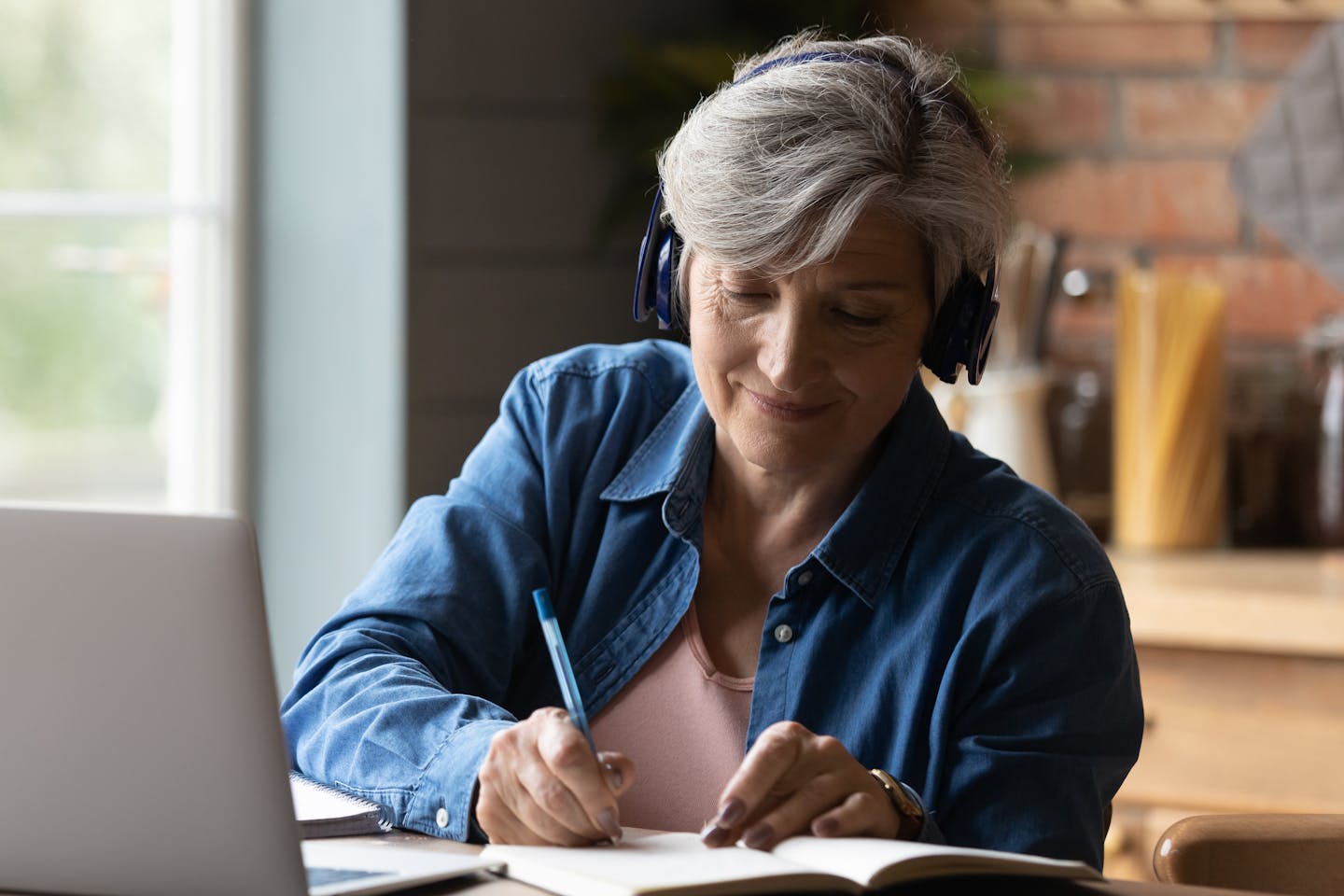 Woman with headphones and laptop taking notes