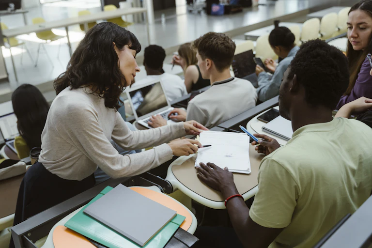 Female teacher assisting male student sitting in lecture hall at university.