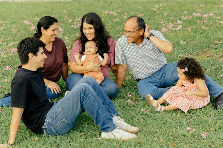 A young couple sits with their young children on the grass with the children's grandparents.