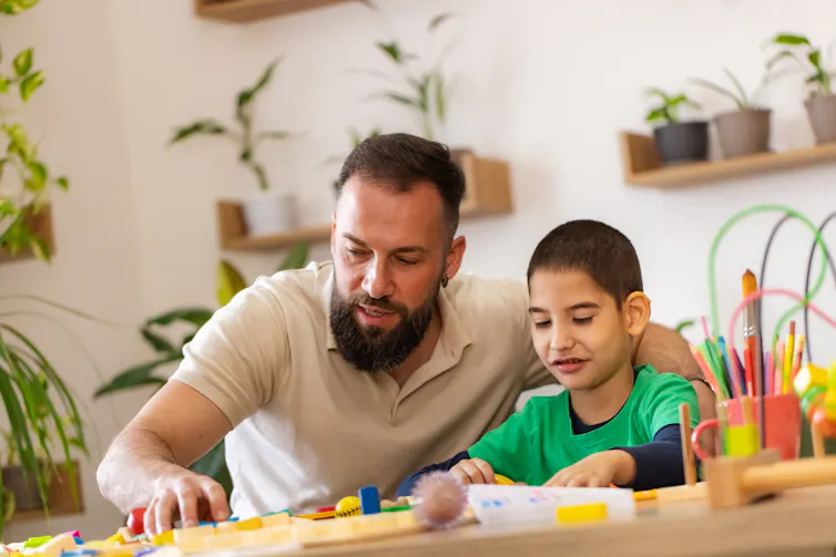 A father and a boy with autism play with toys at a table.