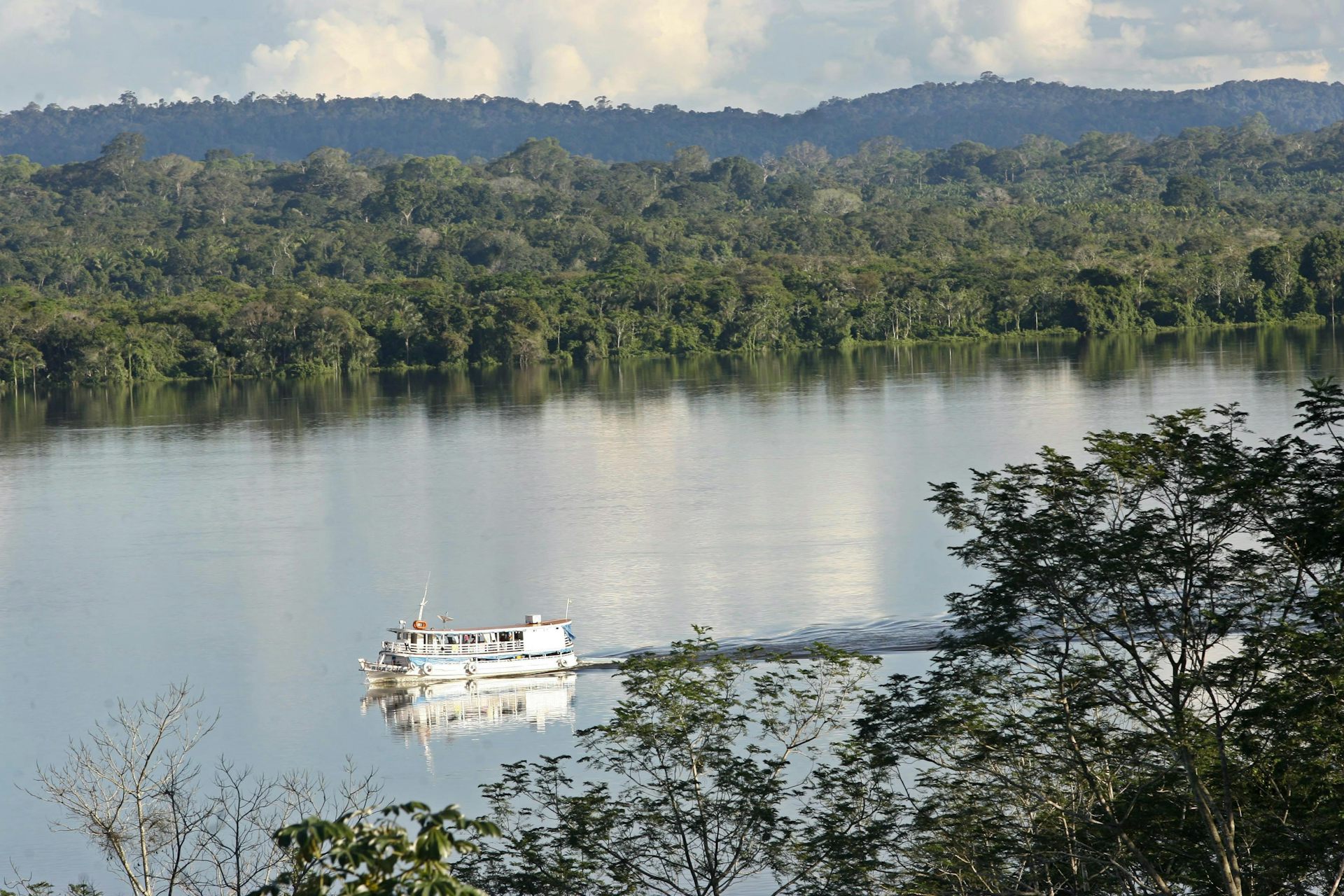 A boat sails along a river surrounded by thick rainforest