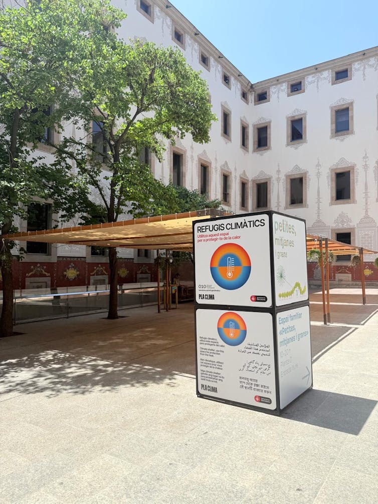 Foto mostra um edifício ao fundo; em primeiro plano, uma praça com toldos para sombra e um grande bloco escrito