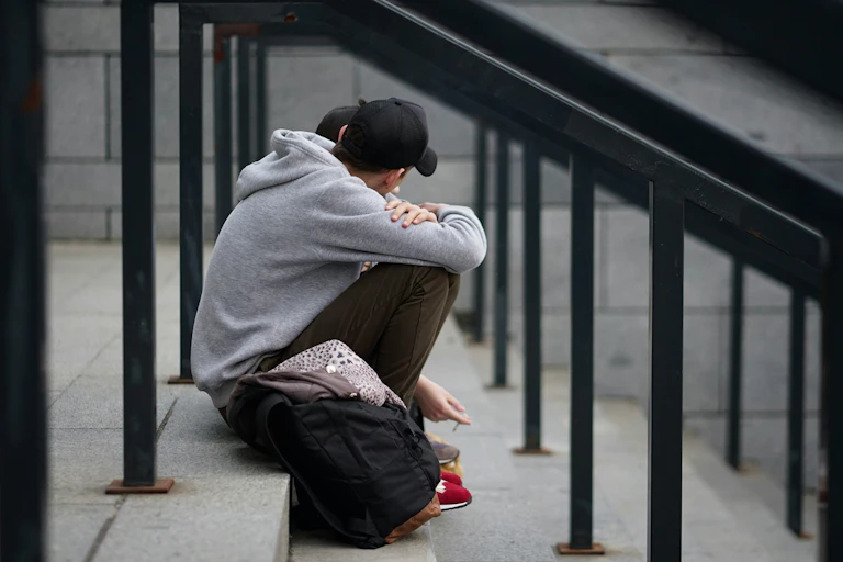 Boy in grey hoody sits on stairs.