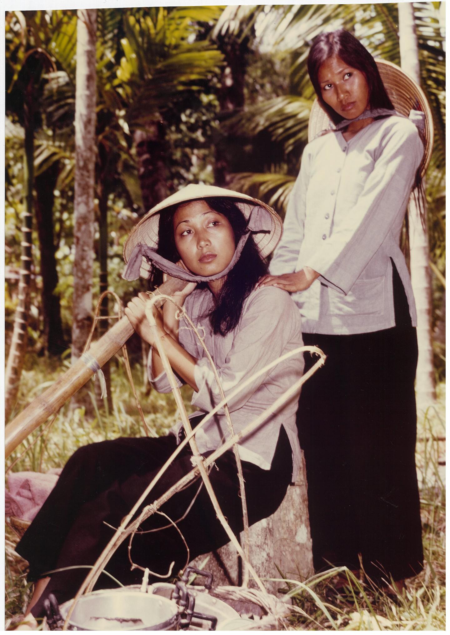 Two figures in the forest, looking away from the camera. Both wear Vietnamese clothing.