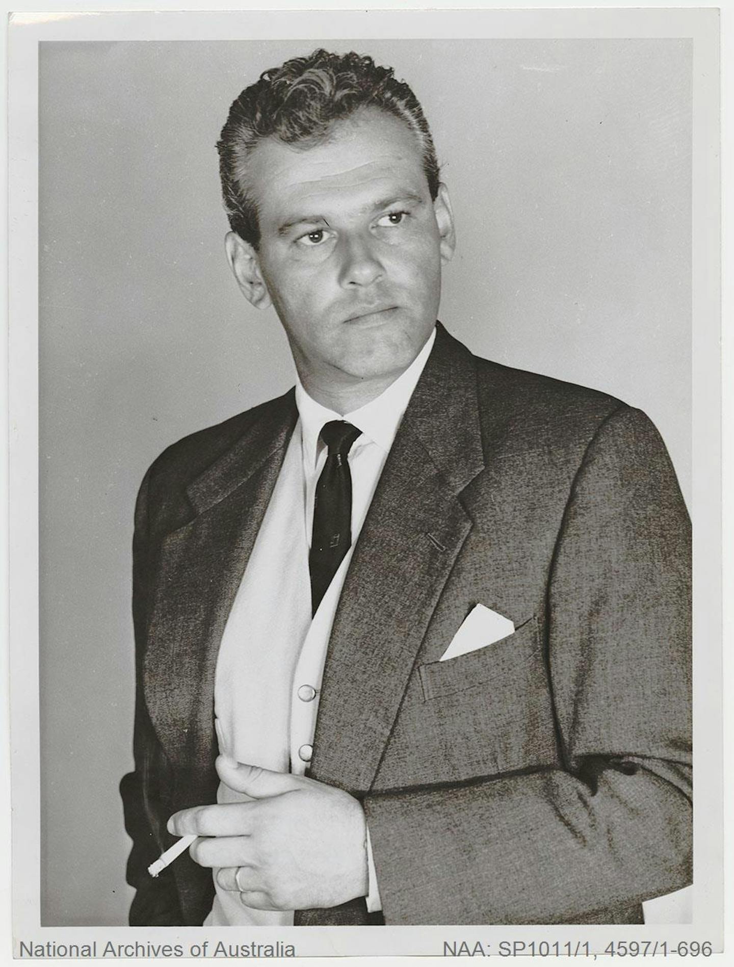 A man poses for the camera in a dinner suit, holding a cigarette.