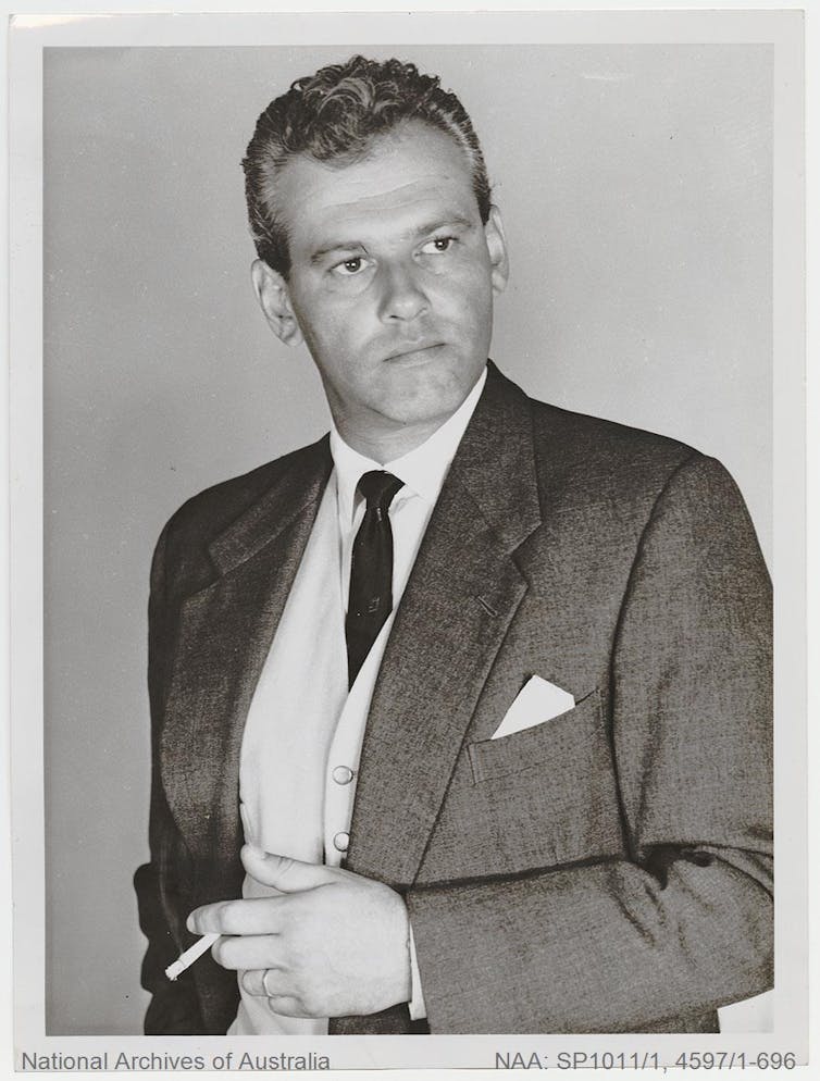 A man poses for the camera in a dinner suit, holding a cigarette.