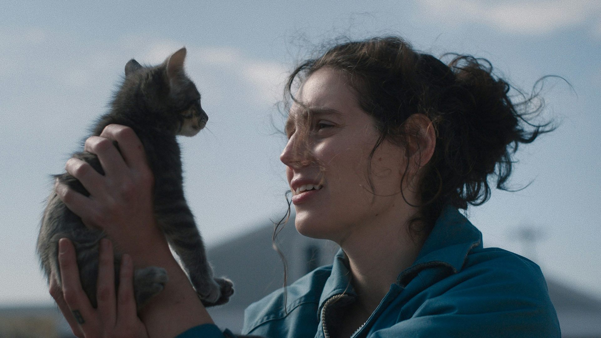 A young woman holding up a kitten and staring into its face.
