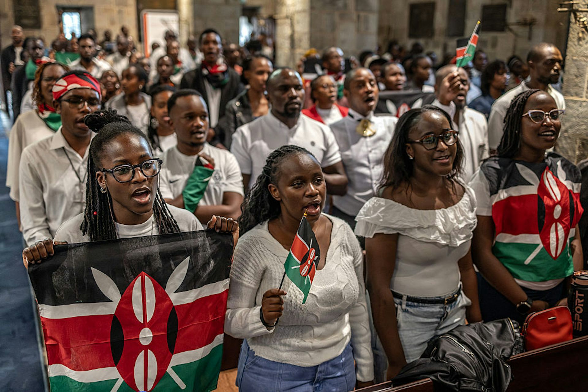 Young people in white T-shirts standing and holding up black, white, red and green flags 