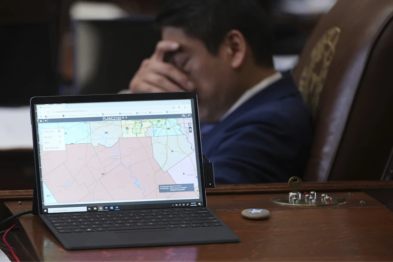 A man sits in a tall leather chair, hand over his eyes, with a laptop showing a map in the foreground.