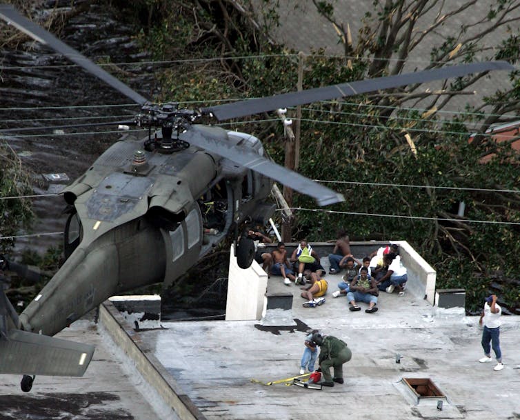 A helicopter hovers above a rooftop with people on it.