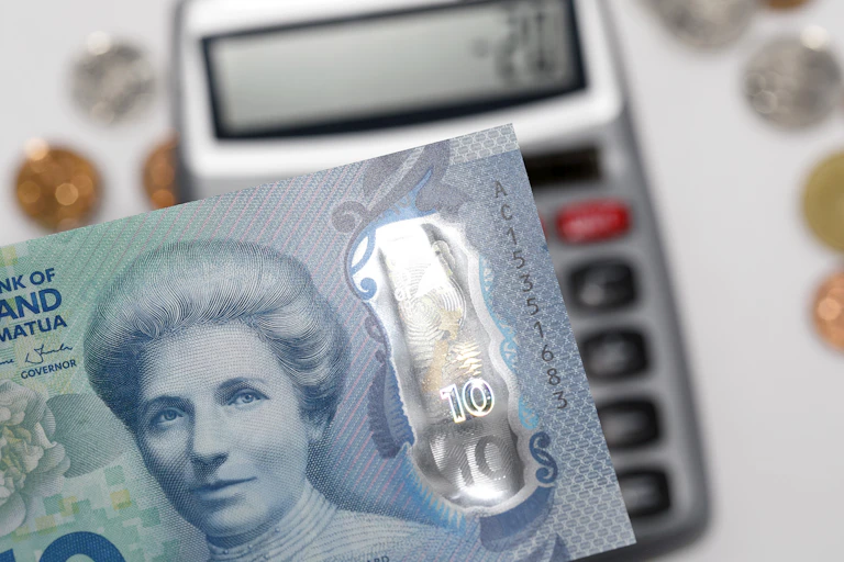 Ten dollar note with enhanced counterfeit resilience over a calculator with mixed New Zealand coins.