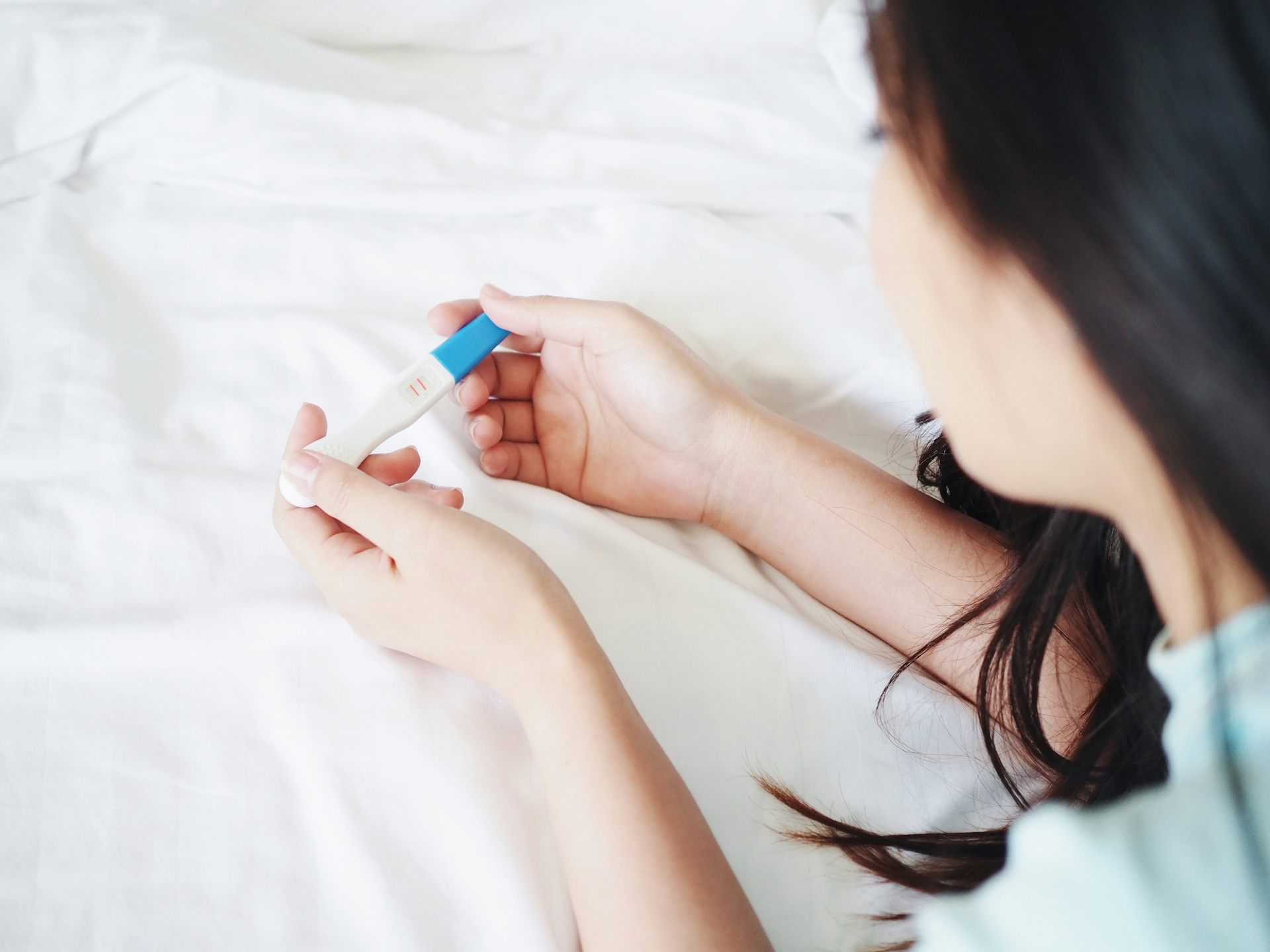 Une jeune femme de dos tient dans ses mains un test de grossesse.