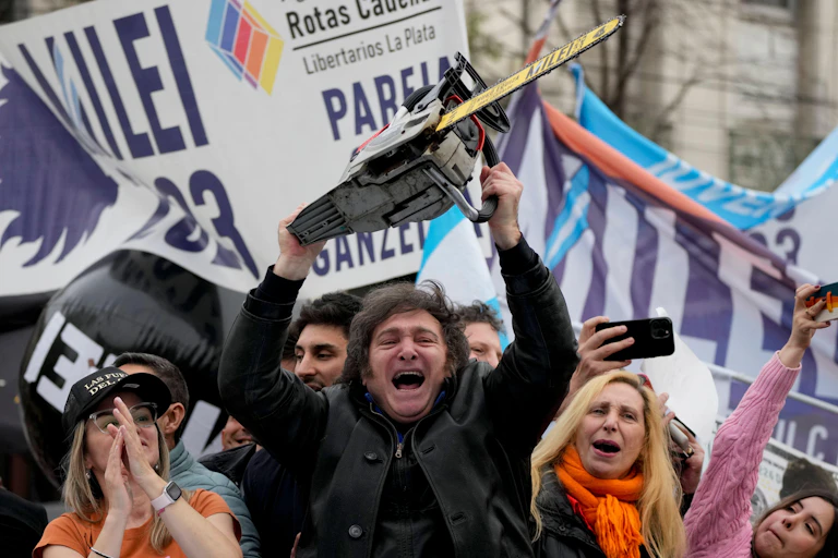 A crazed-looking man brandishing a chainsaw amongst a crowd of supporters at a political rally.