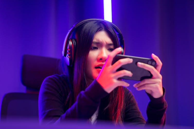 Woman holding her phone and wearing headphones, focusing on a game