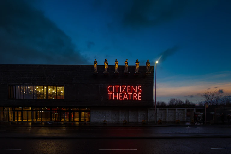 The new frontage of Glasgow's Citizens Theatre against a fading blue sky at dusk, complete with statues on the roof and neon red signage.