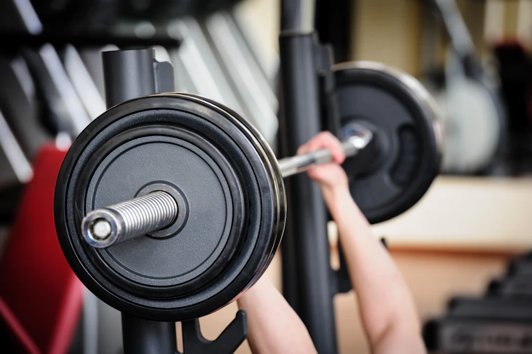 Two hands lift a large barbell in a gym.
