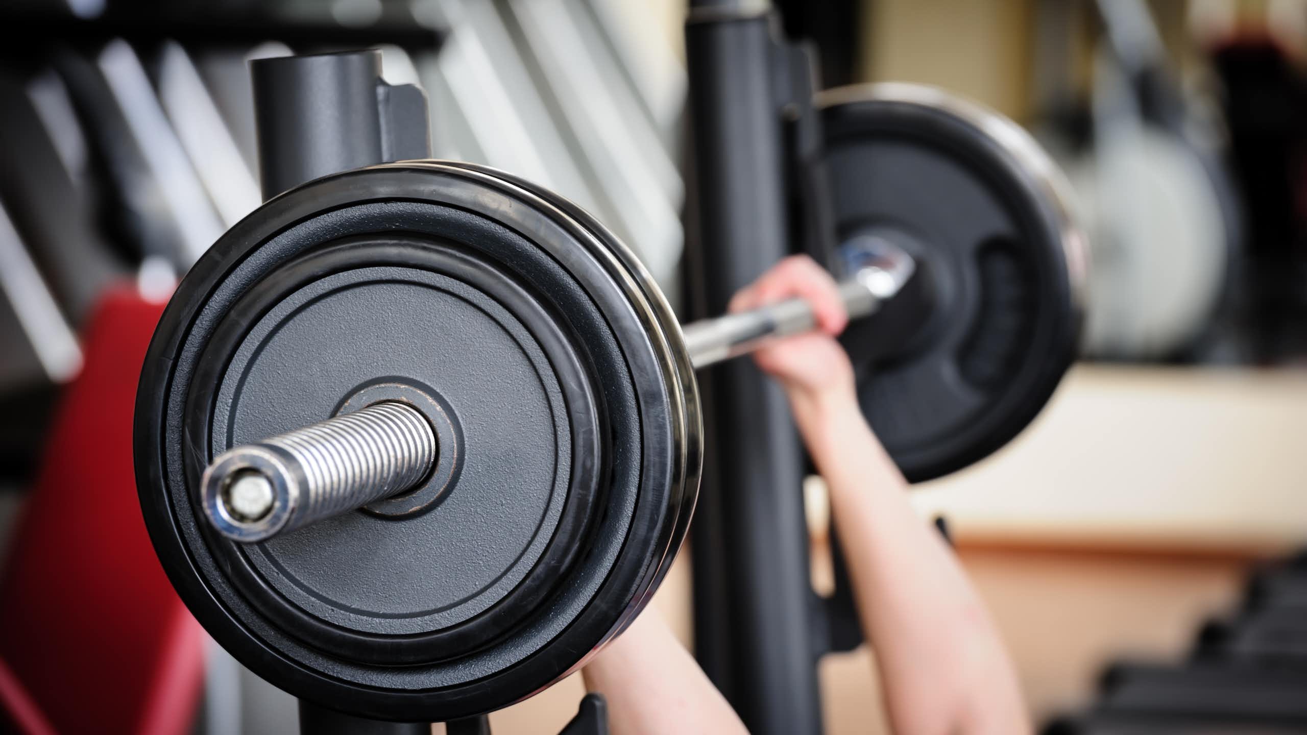 Two hands lift a large barbell in a gym.